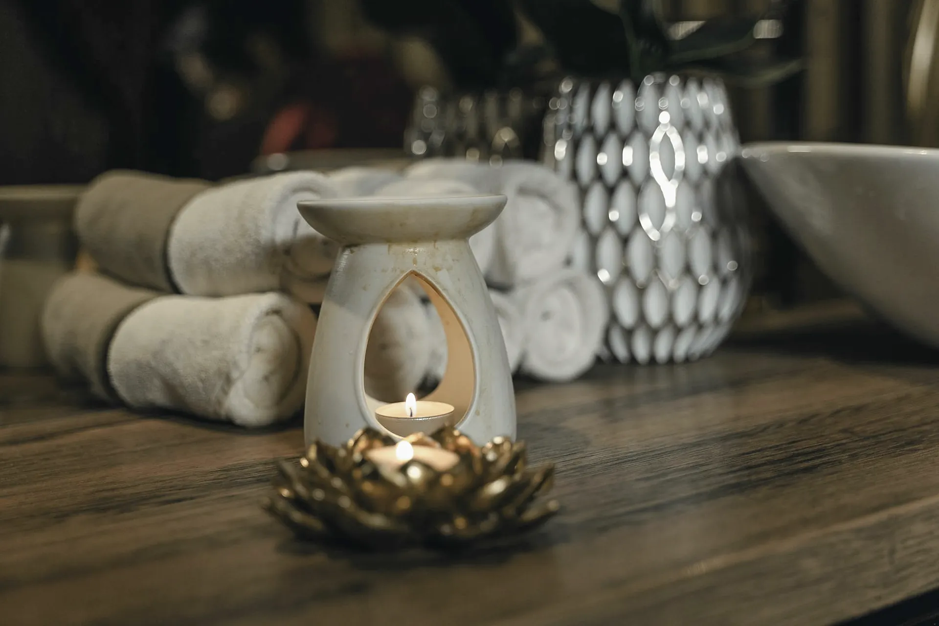 Difusor de aromas sobre un portavelas de loto dorado, junto a toallas enrolladas